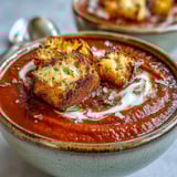 Roasted red pepper soup ladle from a rustic pot, finished with fresh herbs.