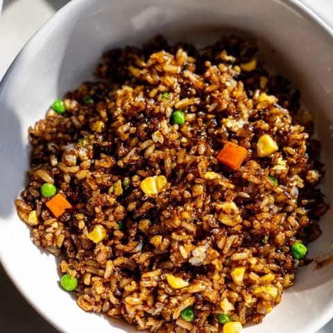 A close-up of Black Garlic Fried Rice in a black wok, garnished with sliced scallions and steaming aromatically from the skillet.