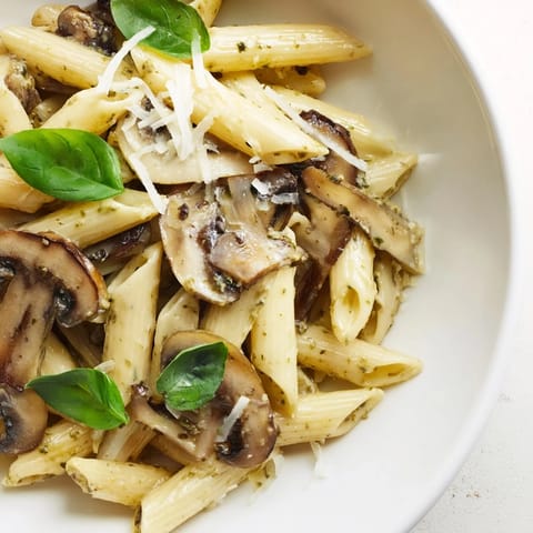 Steaming bowl of homemade mushroom pesto pasta with penne, rich green sauce, and grated Parmesan cheese.