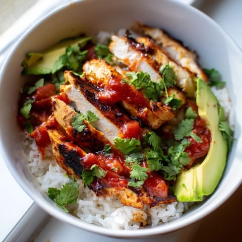 Bright Spicy Chicken Burrito Bowl topped with avocado slices and cilantro next to lime wedges.  