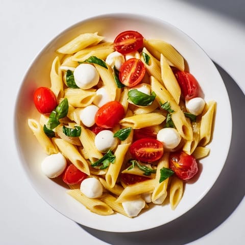 A vibrant bowl of Caprese Salad Pasta, glistening with olive oil and balsamic glaze, served as a light main dish.