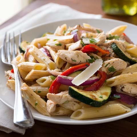 Penne pasta with juicy rosemary-thyme chicken, zucchini, bell peppers, and cherry tomatoes in a skillet, ready to serve.
