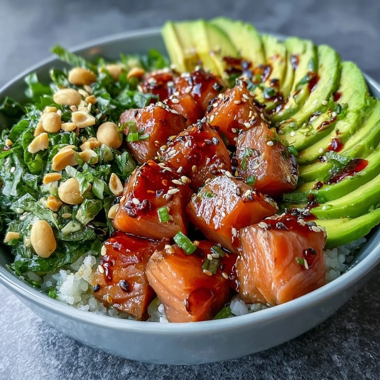Fork-ready cubes of glazed salmon and ripe avocado top a bowl of seasoned sushi rice with peanuts.